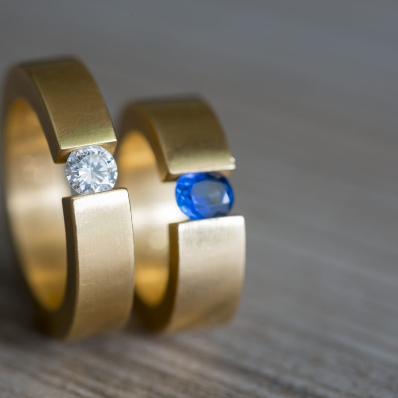 closeup couple golden wedding rings with diamond sapphire wooden table scaled